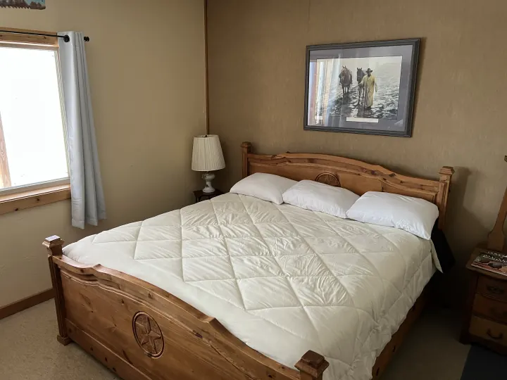 Lodge guest bedroom with a wooden bed and white bedding, photographed in 2022